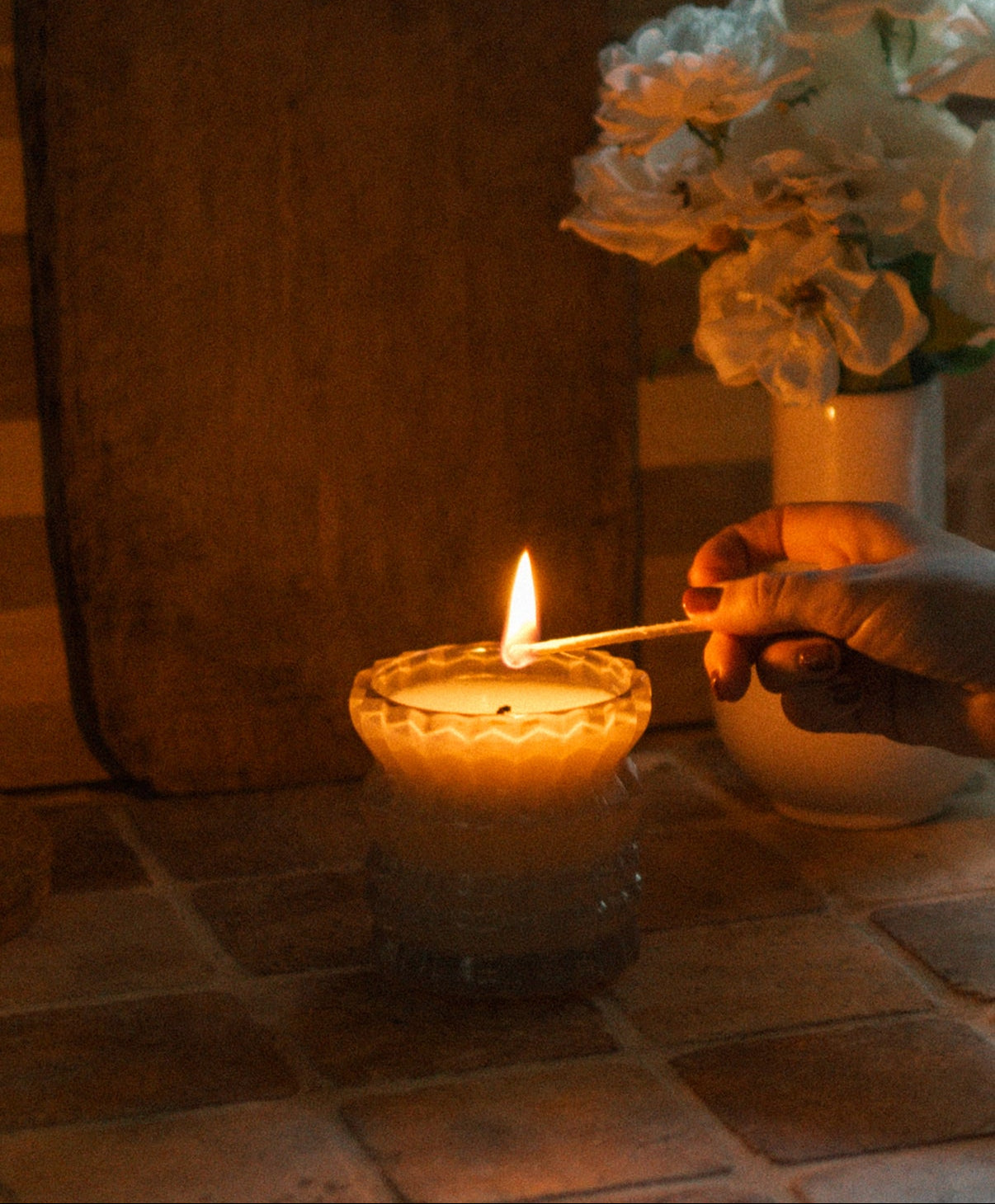 A hand lights the Ellori Non-Toxic Candle in Textured Glass Vessel.