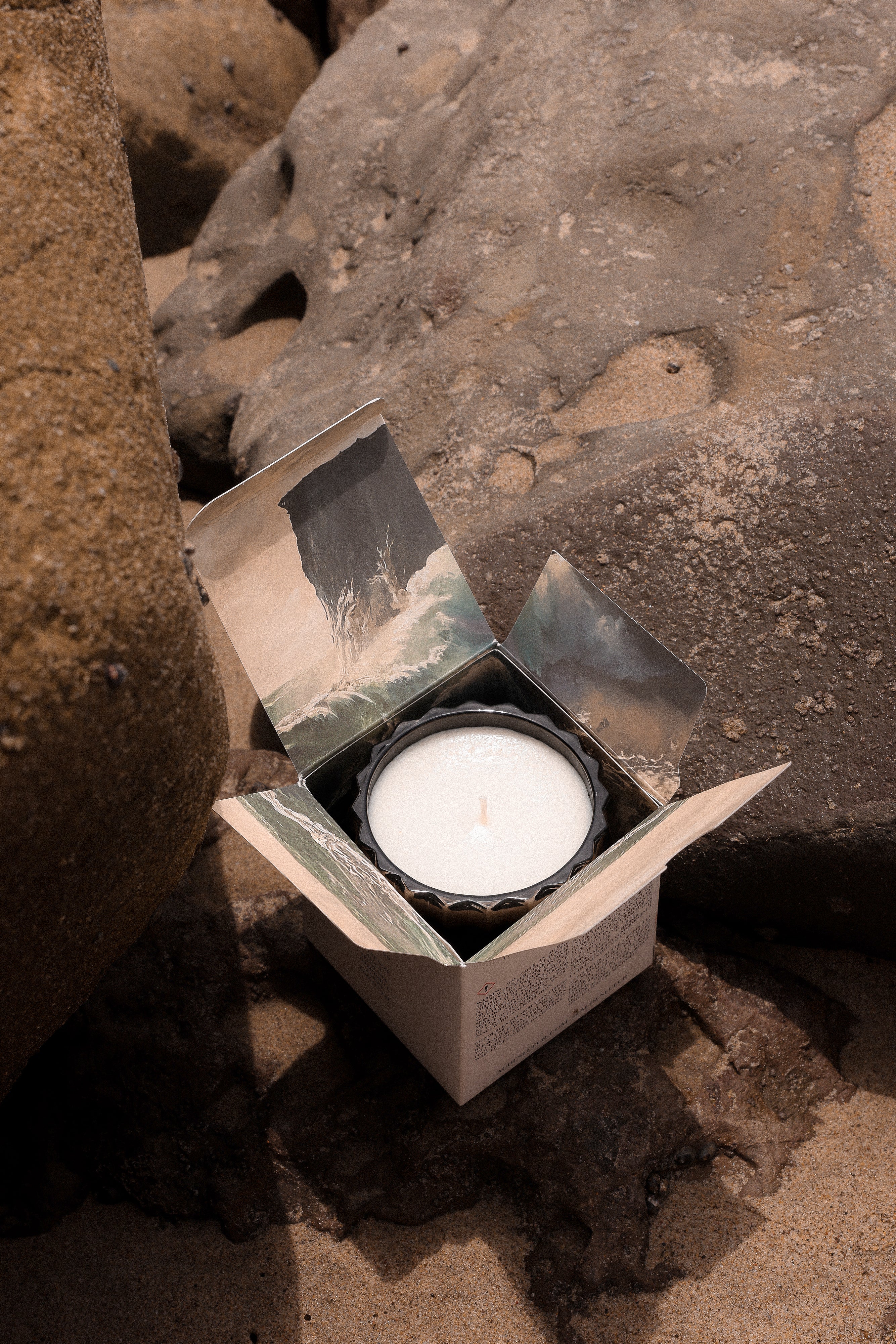 The Maris candle is set on a rock, nestled in its box with the flaps flipped open to reveal the beautiful design inside.