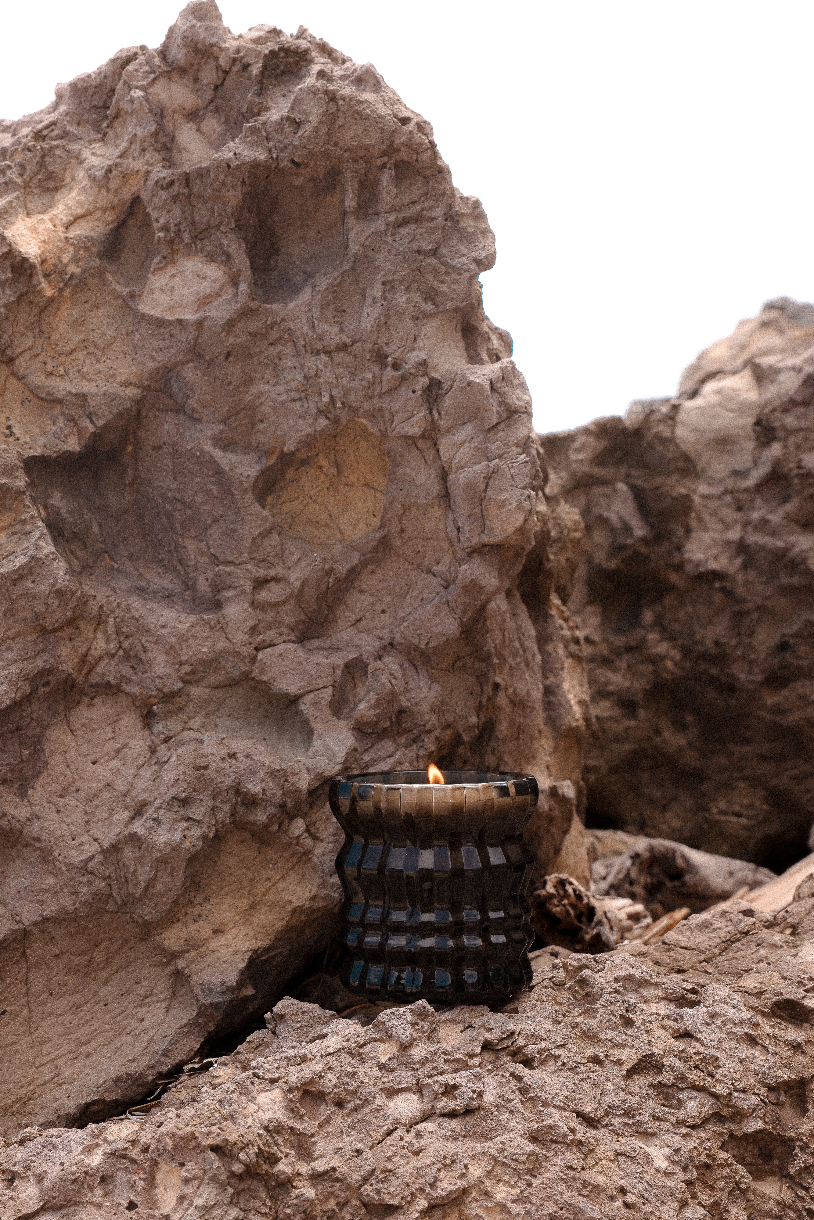 The Maris candle sits on a rock at the beach, its flame flickering.