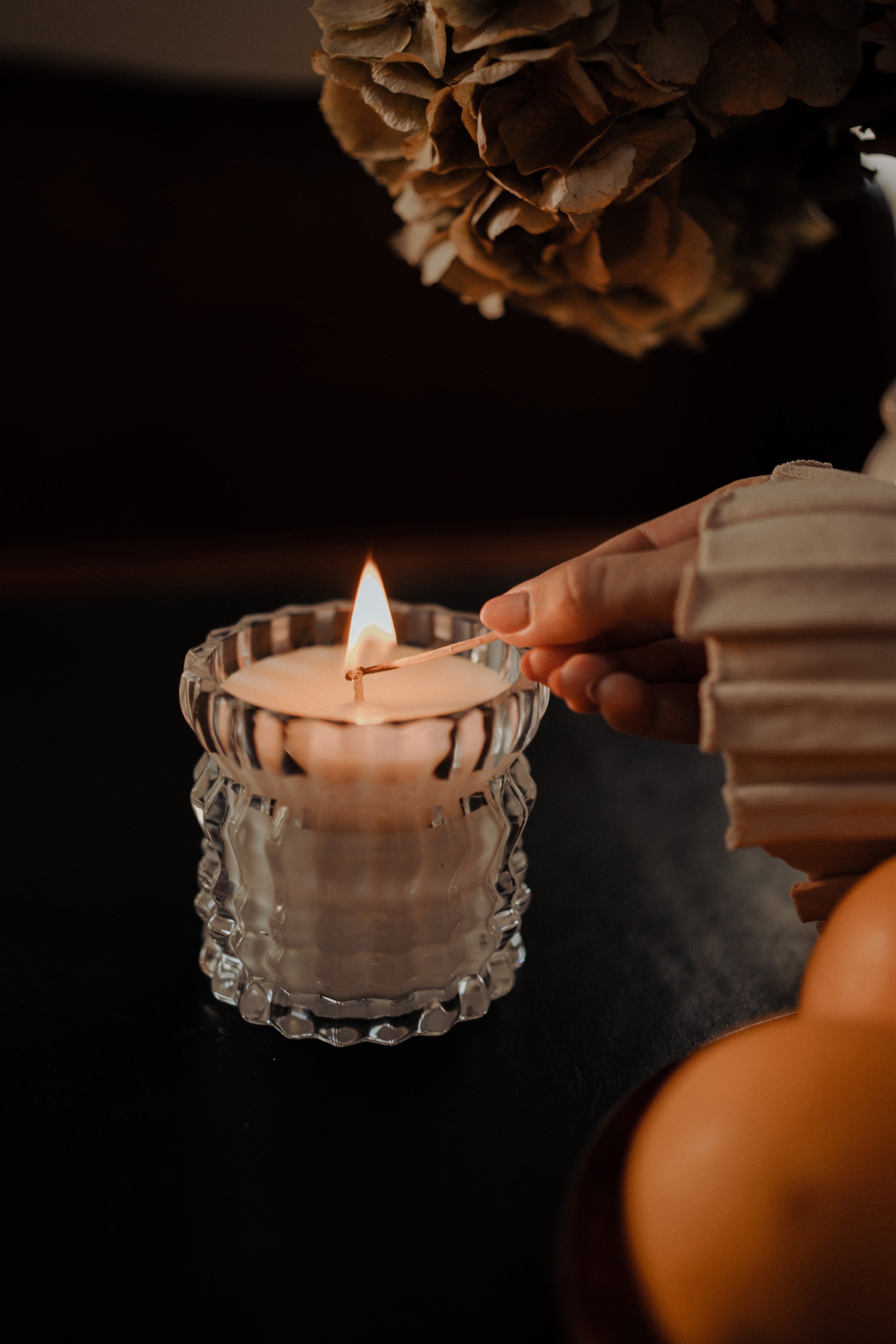 A hand lighting the Arlow candle from Auden Lueur.