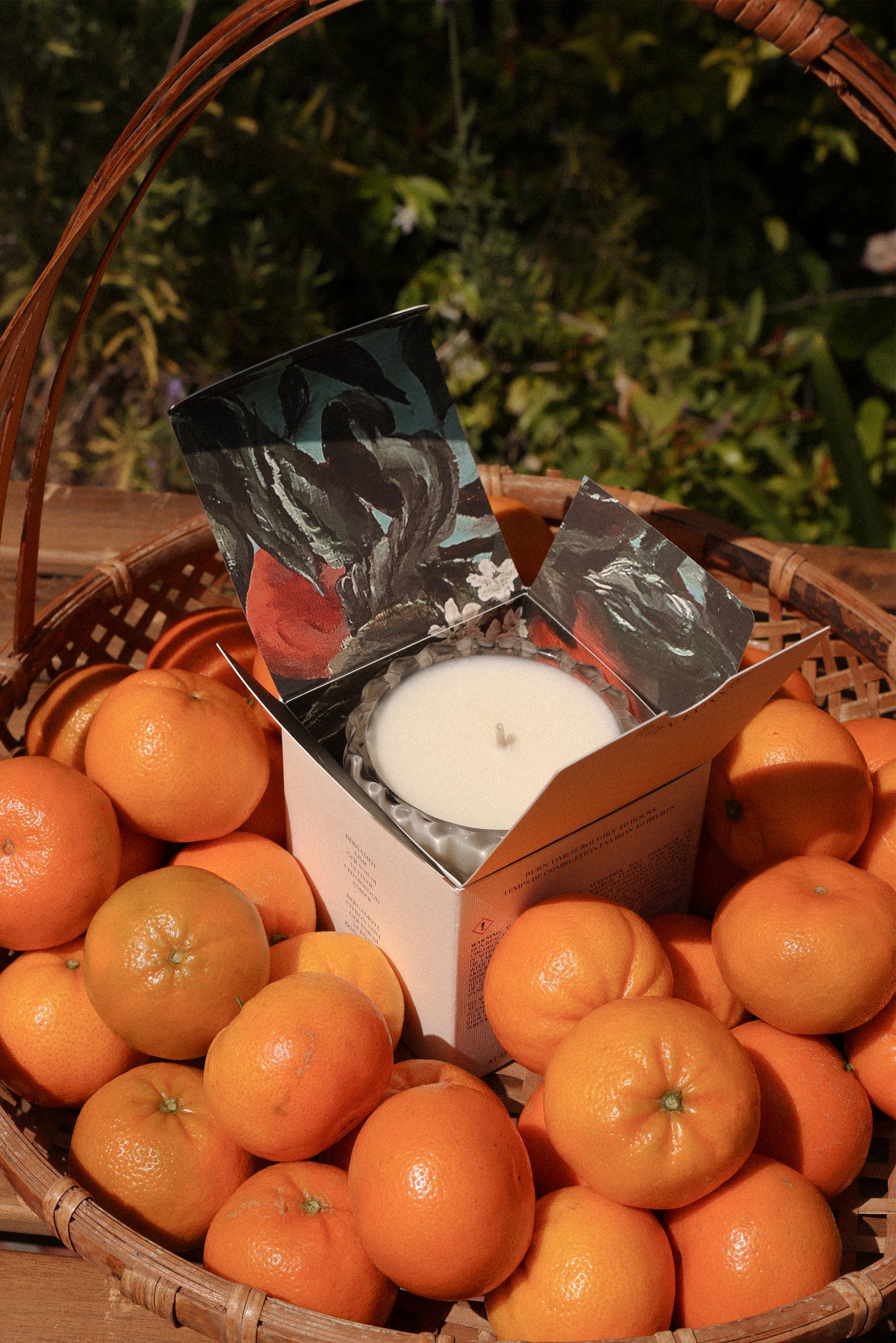The Arlow candle, nestled in its box, rests delicately in a basket of fresh bergamots.