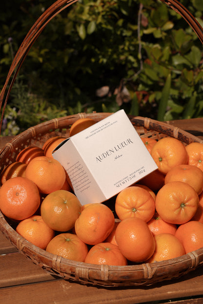 The Arlow candle box packaging rests elegantly in a basket of bergamots.