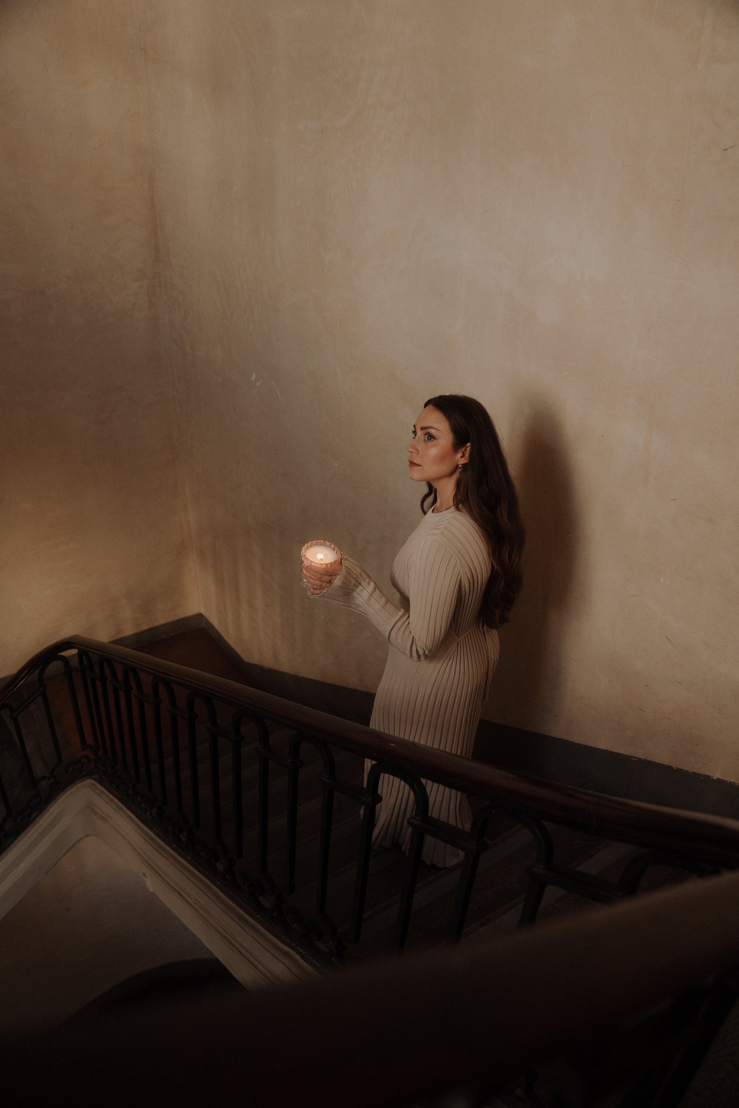 MaCenna Lee of Auden Lueur descends a staircase, holding the Arlow candle alight in her hands.
