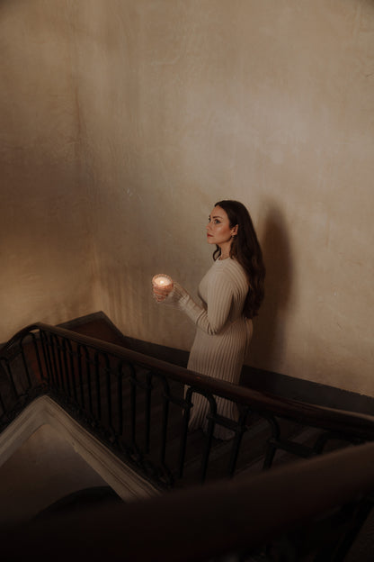 MaCenna Lee of Auden Lueur descends a staircase, holding the Arlow candle alight in her hands.