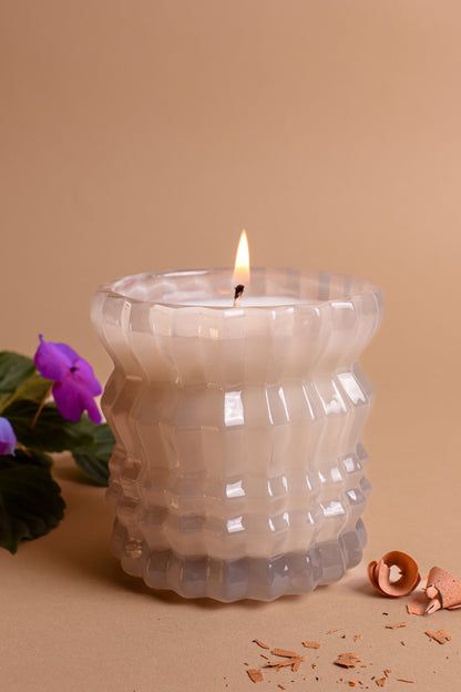 The Ellori Non-Toxic Candle in Textured Glass Vessel displayed next to delicate violet flowers.