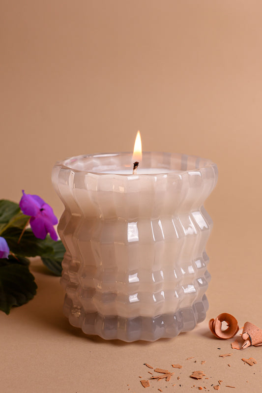 The Ellori Non-Toxic Candle in Textured Glass Vessel displayed next to delicate violet flowers.