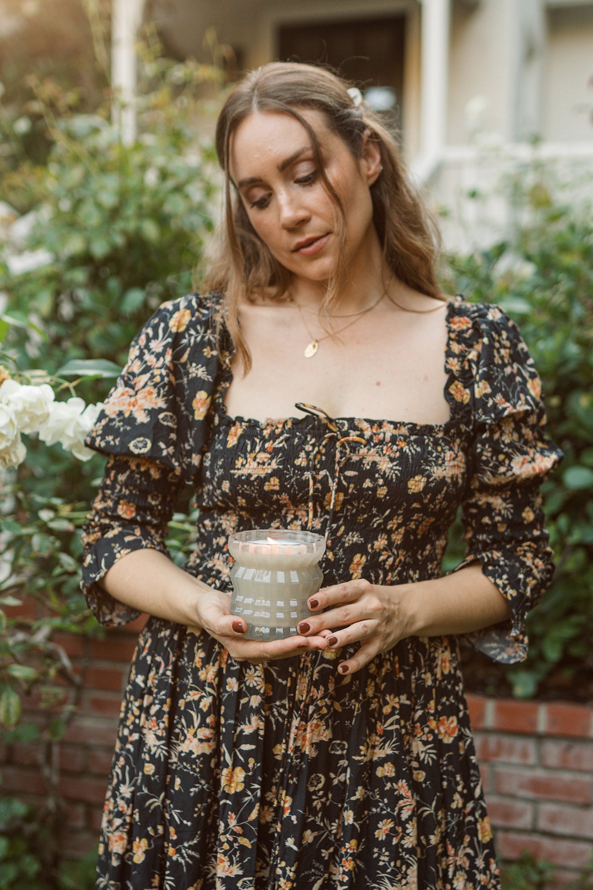 MaCenna Lee holds the lit Ellori candle, surrounded by the beauty of a garden.