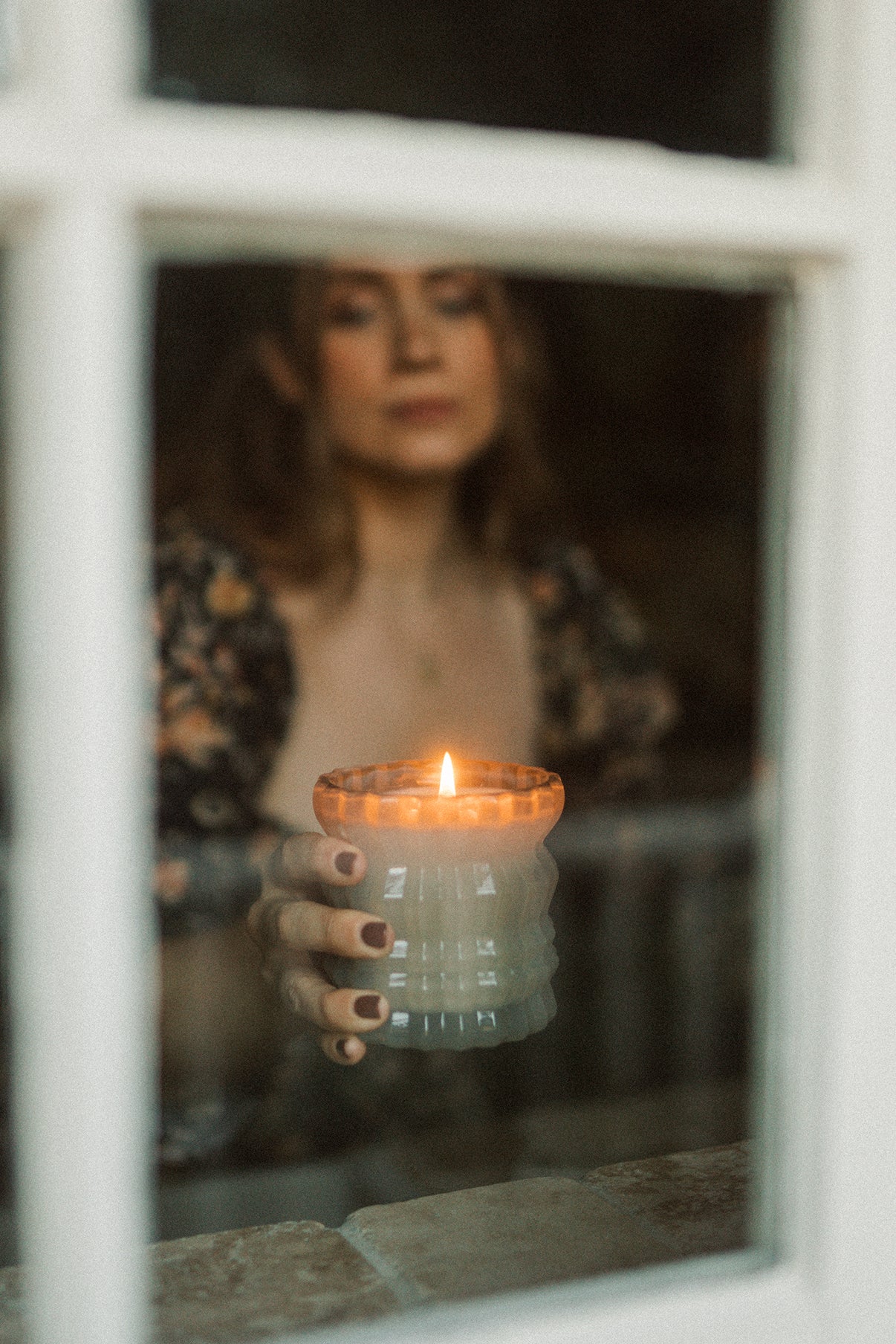 MaCenna Lee holds the lit Ellori candle, gently bringing it toward the windowsill of a house.