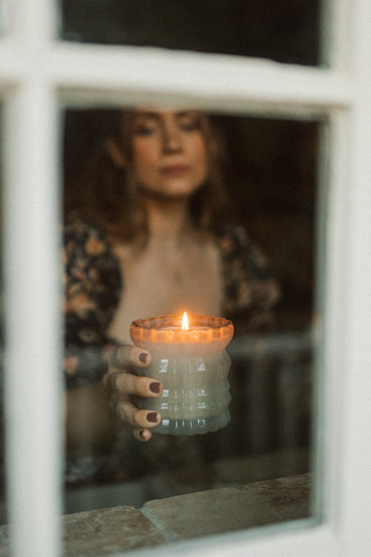 MaCenna Lee holds the lit Ellori candle, gently bringing it toward the windowsill of a house.