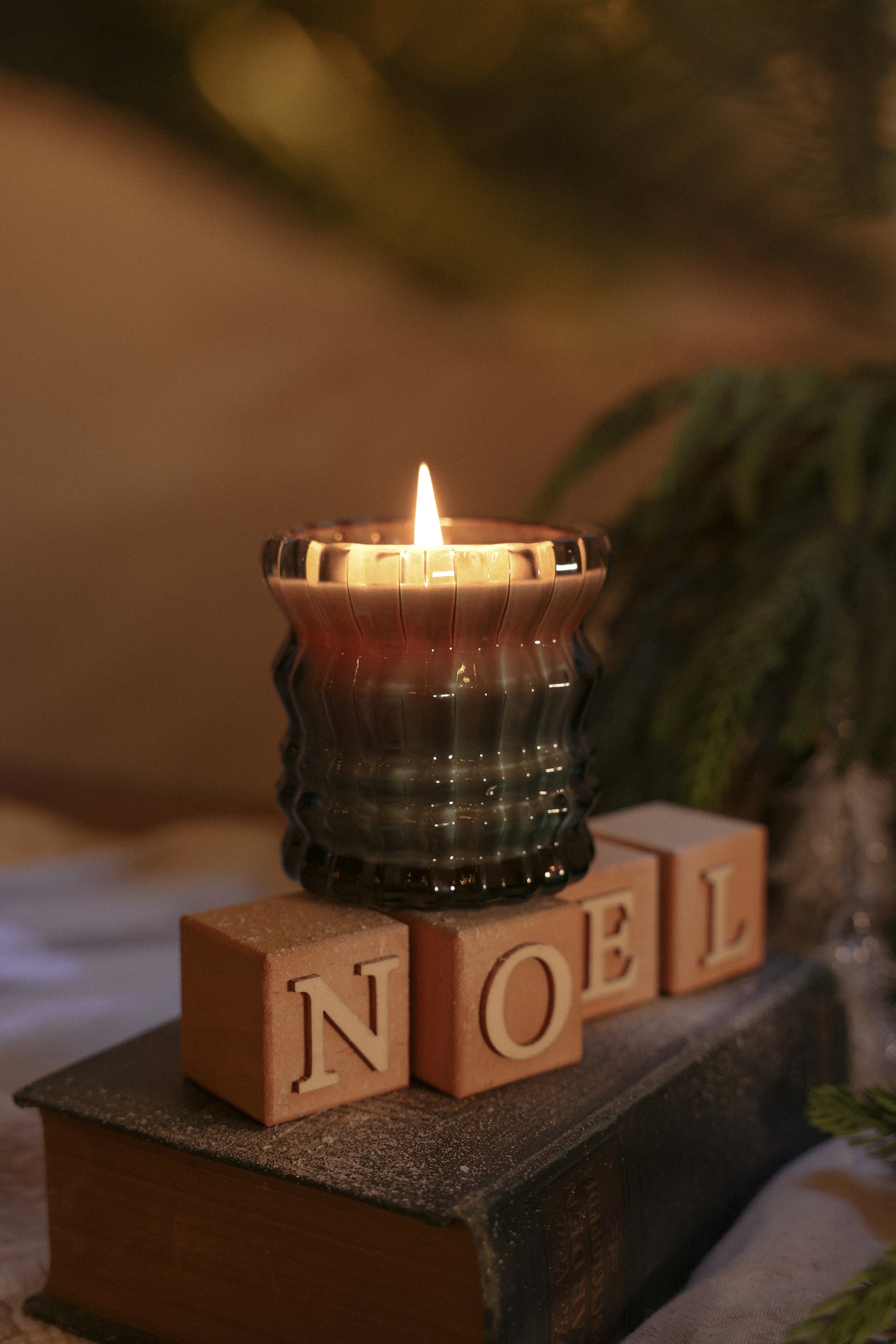 The Noel candle sits atop decorative blocks spelling out "NOEL," resting on a book beneath it.