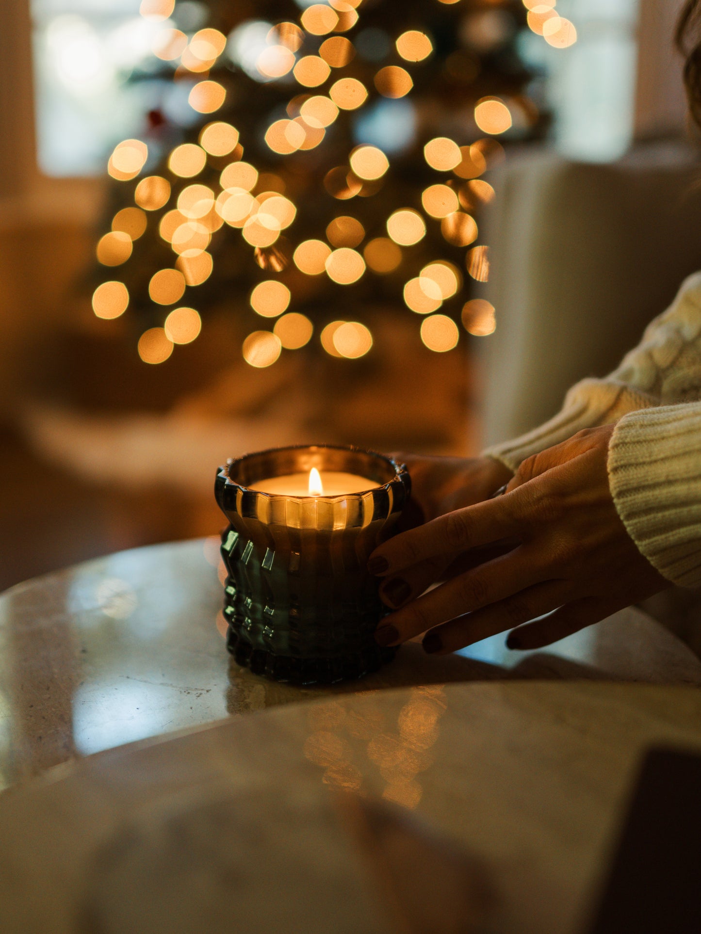 The Noel candle is lit, with a Christmas tree glowing in the background as someone gently touches the candle.