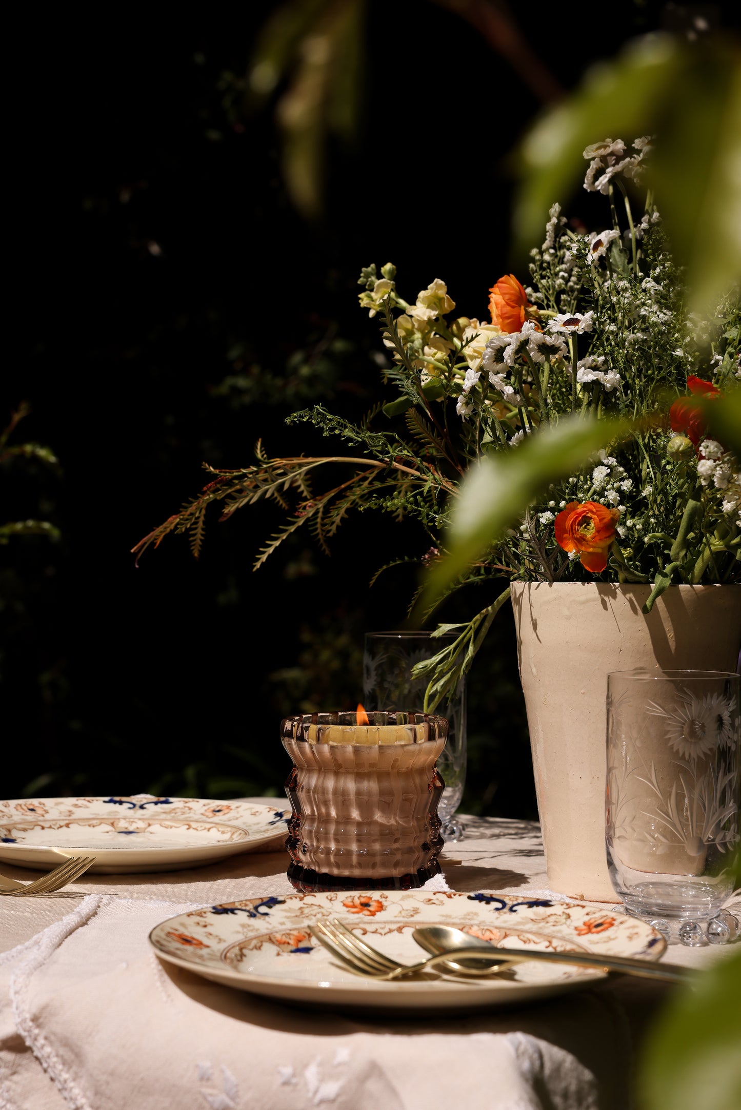 The Willow candle is displayed at a dinner setting, glowing softly in the center of the table.