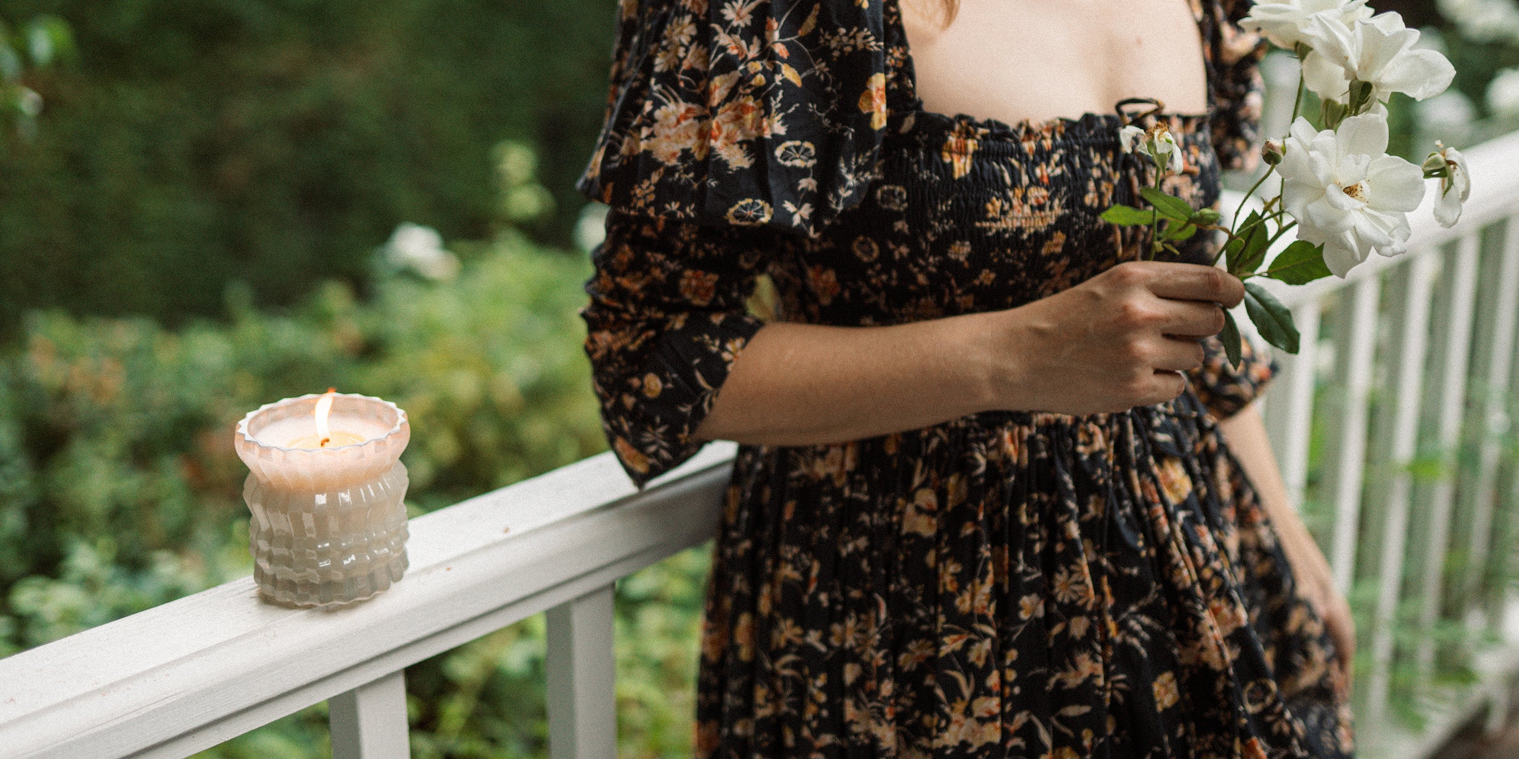 Ellori candle lit on a railing in a serene garden setting.